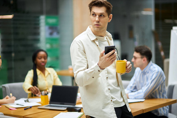 handsome serious man holding smart phone, cup of tea, going to make a phone call - Foto, Imagen