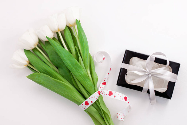 Fiori di tulipano bianco e scatola regalo nera su sfondo chiaro posa piatta. Luogo per il testo 8 Marzo Felice Festa della Mamma delle Donne
. - Foto, immagini
