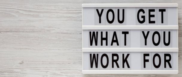 "Du bekommst, wofür du arbeitest" Worte auf einem Leuchtkasten auf weißem Holz - Foto, Bild