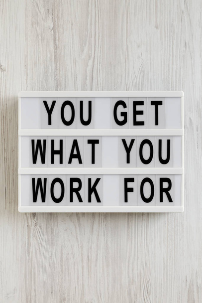 'You get what you work for' words on a lightbox on a white wooden surface, top view. Overhead, from above, flat lay. Space for text. - Foto, Imagem