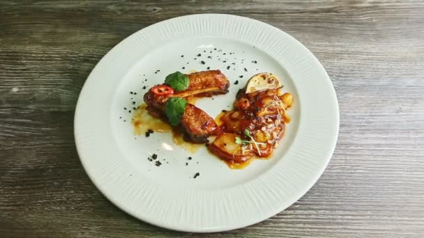 fork and knife above fried meat ribs with sauce and garnish on white plate - Video, Çekim