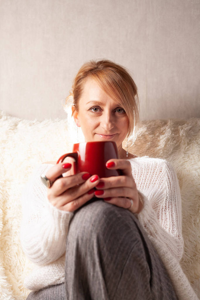 Aikuisen naisen muotokuva kodikkaassa huoneessa sohvalla kupin teetä / kahvia kanssa
. - Valokuva, kuva