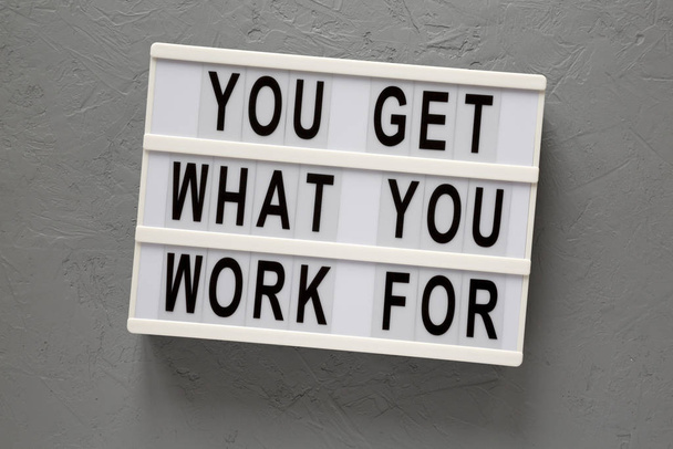 'Je krijgt waar je voor werkt' woorden op een lichtbak op een grijze surfac - Foto, afbeelding