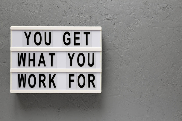 'Usted consigue lo que usted trabaja para' palabras en un tablero moderno en una ba gris
 - Foto, Imagen
