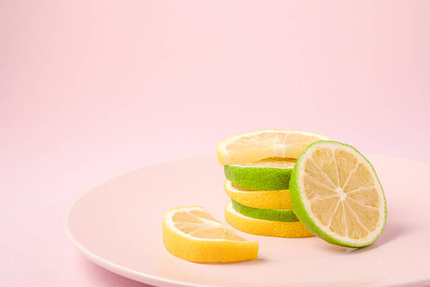 Świeże smaczne plastry cytryny i owoców cytrusowych limonki ułożone na różowym talerzu, odizolowane minimalne tło, widok kątowy, makro - Zdjęcie, obraz