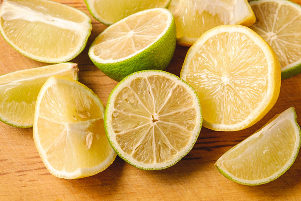 Fresh tasty lemon and lime citrus fruits slices on wooden cutting board, top view macro - Photo, Image