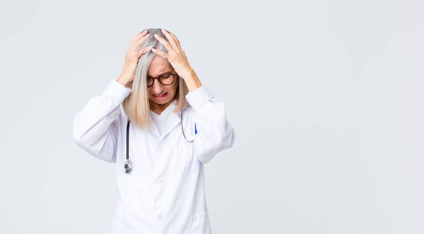 中年の医者の女性はストレスと不満を感じ頭に手を上げ疲れを感じ不満を感じ片頭痛で - 写真・画像