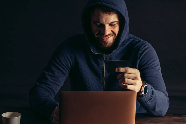 smiling hacker man sit holding bank card - Photo, Image