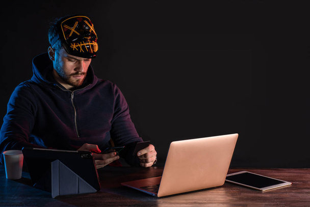 jonge Kaukasische hacker mannelijke zitten met laptop en smartphone - Foto, afbeelding