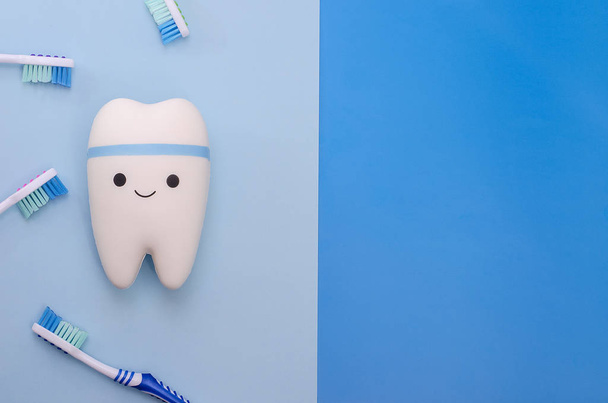 Cheerful smiling tooth on a blue background with toothbrushes with copy space. Pediatric and adult dentistry. Dental treatment and whitening.  - Φωτογραφία, εικόνα