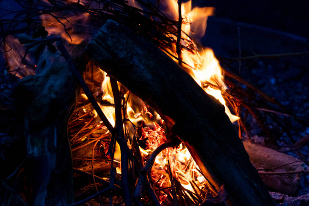 Glanzend brandend vuur in het donker toont de romantische kant van een kampvuur of kampvuur, brandveiligheid en de noodzaak van een brandverzekering, evenals overlevingsavonturen buiten met de kinderen en het gezin - Foto, afbeelding