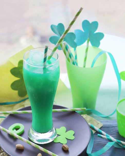 St. Patrick Day, glasses with a green drink, cocktail tubes with a decorative shamrock, clover on a wooden surface on a window background, getting ready for a party - Photo, Image