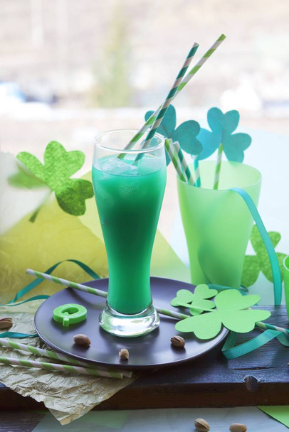 Dia de São Patrício, copos com uma bebida verde, tubos de coquetel com um trevo decorativo, trevo em uma superfície de madeira em um contexto de janela, preparando-se para uma festa
 - Foto, Imagem