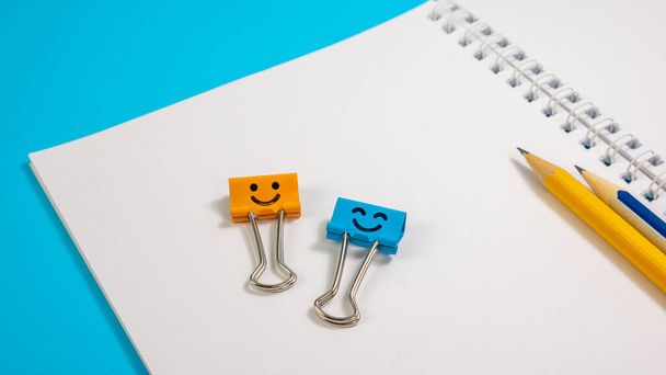 Clips de reliure sourire avec crayons jaunes et bleus sur bloc-notes
 - Photo, image
