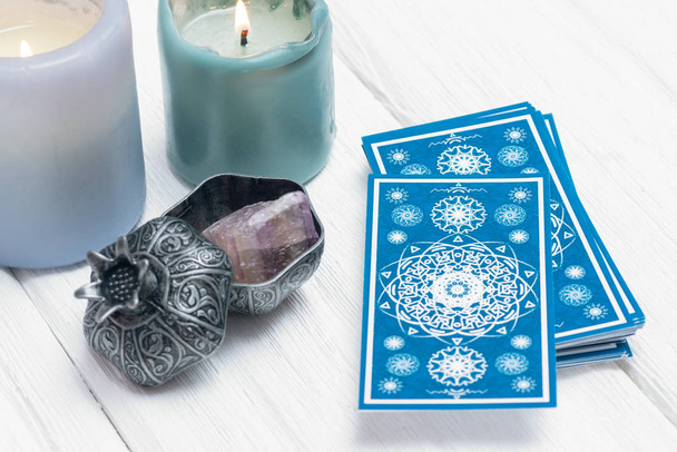 Blue tarot cards and burning candle on white table background. - Фото, изображение