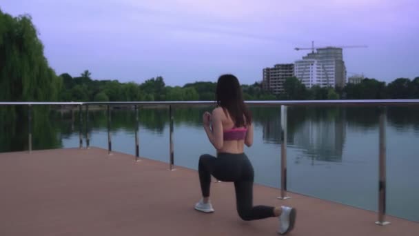 Fitness woman doing lunges on lake pier. - Кадры, видео
