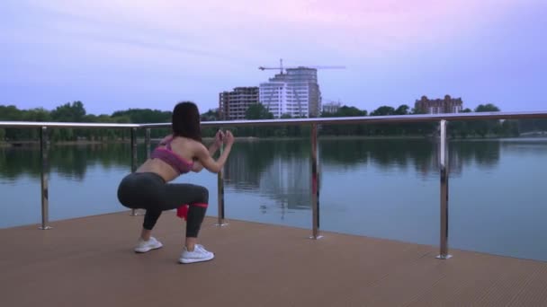 Fitness woman doing squats on lake pier. - Video