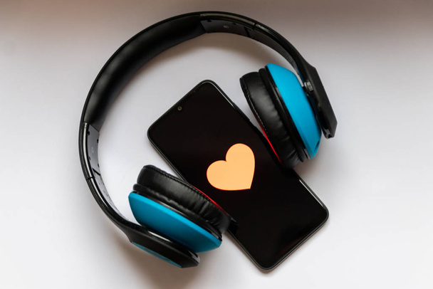 Černý smartphone s červeným srdcem na černé obrazovce a bezdrátové modré přes sluchátka show mobilní hudba streaming, kontrola zdraví, smartphone závislost, láska k hudbě a poslech hudby - Fotografie, Obrázek