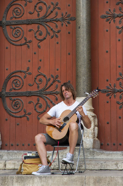gitarzysta siedzący przy drzwiach kościoła w wiosce Arles - Zdjęcie, obraz