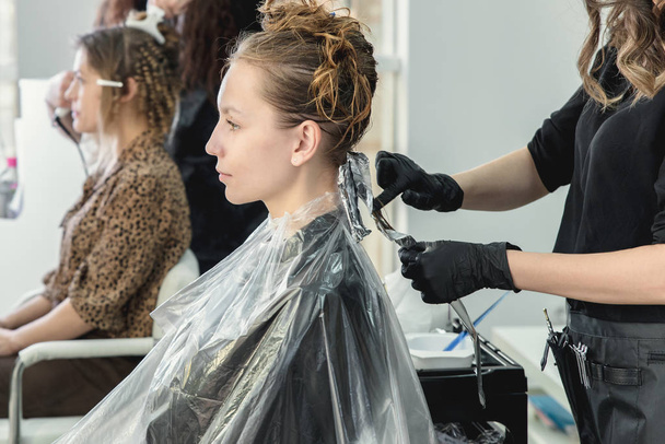 Hairdresser coloring young woman hair using foil - Fotó, kép