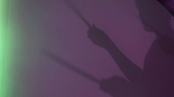Seitenansicht des jungen Schlagzeugers Silhouette mit Schlagzeug-Stick auf lila Wand Hintergrund. Konzept. Männlicher Schatten, der vorgibt, unter Neonlicht der Lampen zu trommeln, Musik und Kunstkonzept. - Foto, Bild