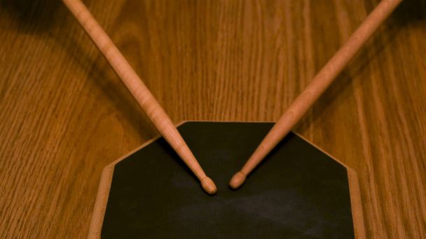Primer plano de un hombre o una mujer practicando sobre una almohadilla de tambor con palos de tambor sobre un fondo de mesa de madera. Concepto. Una persona está entrenando para batir el ritmo
. - Foto, imagen