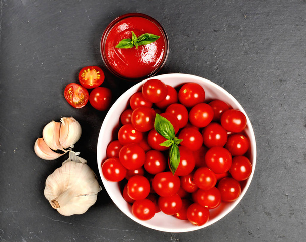 Ketchup casero hecho de tomates cherry frescos, ajo, albahaca en losa de pizarra negra. Vista superior
. - Foto, imagen