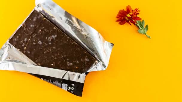 Stop motion video of disappearing Dark Almond and Salty Caramel Chocolate bar and orange daisy photographed against orange background - Кадры, видео