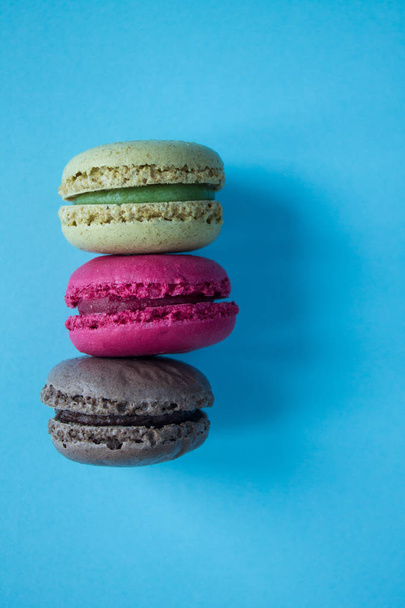 Three macaroons: pistachio, raspberry and chocolate on a blue background with copy space. Food photo. - Φωτογραφία, εικόνα