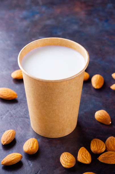 Almond milk with almond on dark background. Homemade organic almond milk in a paper cup for healthy breakfast. Vegan milk from almonds nuts in kraft paper cup. Alternative milk. Zero waste - Fotoğraf, Görsel