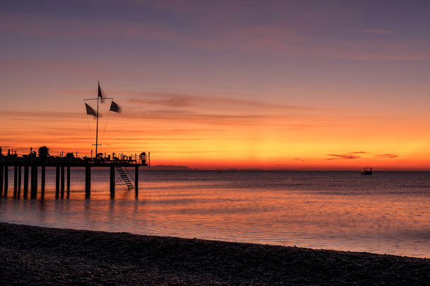 Middellandse Zee zonsopgang met kiezelstrand en pier silhouet - Foto, afbeelding