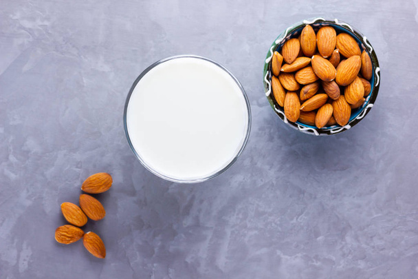 Almond milk with almond on gray background. Homemade organic almond milk in a glass for healthy breakfast. Vegan milk from almonds nuts on a cement. Alternative milk. Top view. Copy space - Zdjęcie, obraz