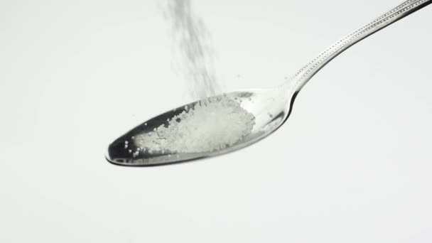 Biała granulowana łyżeczka cukru spada na białe tło w zwolnionym tempie - Materiał filmowy, wideo