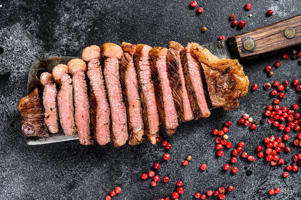 Grilled strip loin steak on a cleaver. The cooking medium. Black background. Top view - Photo, Image