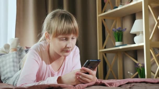 Blonde girl uses a smartphone in her bedroom - Materiał filmowy, wideo