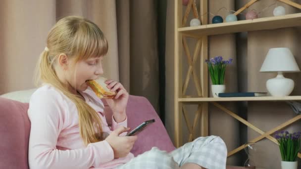 Girl uses smartphone and has a sandwich in her bedroom - Materiał filmowy, wideo