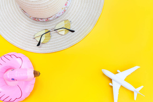 夏のビーチ組成物。飛行機のサングラスの帽子と黄色の背景に隔離されたインフレータブルフラミンゴと最小限のシンプルなフラットレイ。休暇旅行アドベンチャー旅行のコンセプト。トップ表示コピースペース. - 写真・画像