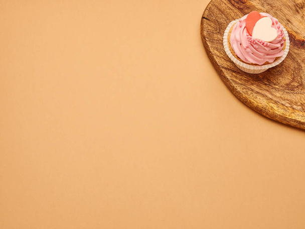 Pink cupcakes cakes with hearts on a kitchen wooden board on a beige brown background - Foto, afbeelding
