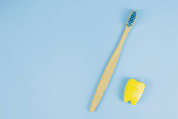 Bamboe houten borstel en tandzijde in de vorm van een tand op een blauwe achtergrond. Orale zorg concept. Kopieerruimte - Foto, afbeelding