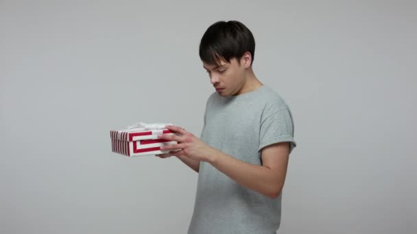 Wow, I like present! Happy lucky brunette man in T-shirt unpacking long-awaited gift box and looking amazed overjoyed, satisfied with birthday surprise. indoor studio shot isolated on gray background - Footage, Video