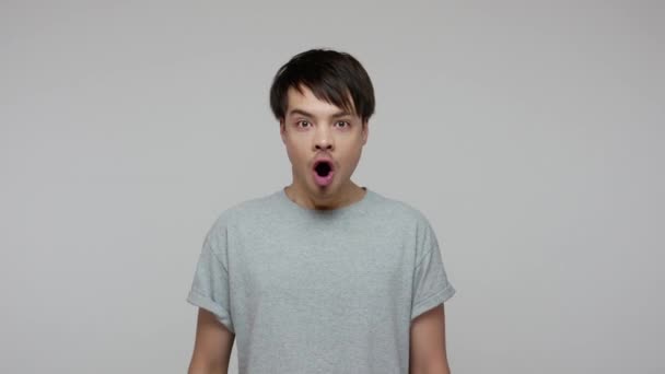 Overjoyed excited guy in T-shirt suddenly hearing amazing news and opening his mouth wide in surprise, shocked by lottery winning, unbelievable success. indoor studio shot isolated on gray background - Séquence, vidéo