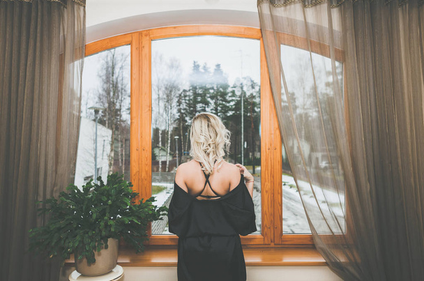 Egy nő néz be a régi ablakon, az ablakpárkányon ülve. Harisnyába öltözve - Fotó, kép
