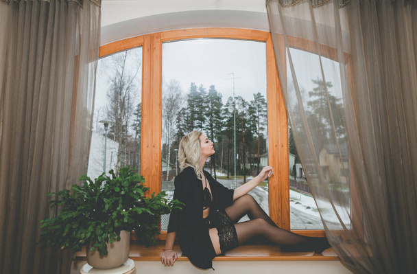 Γυναίκα κοιτάζει μέσα από το παλιό παράθυρο κάθεται στο περβάζι του παραθύρου. Ντυμένες με κάλτσες - Φωτογραφία, εικόνα