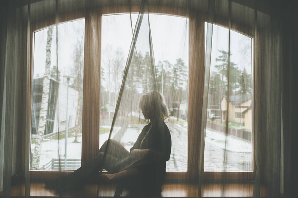 Silueta chica rubia sentada en el alféizar de la ventana
 - Foto, Imagen