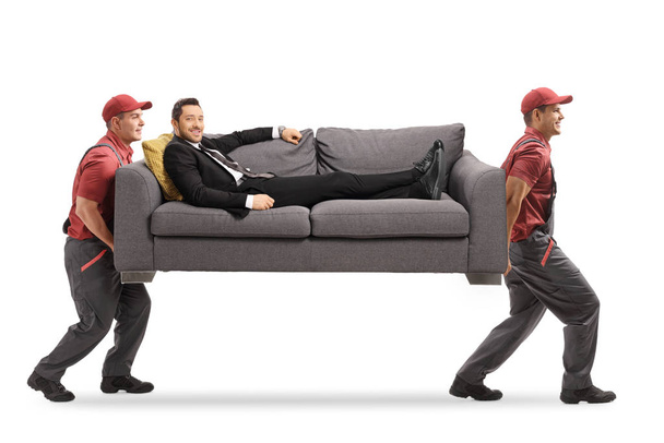 Movers carrying a sofa with a man in a suit relaxing on the sofa - Foto, Bild