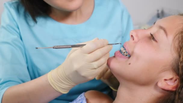 Ortodoncista femenina examinando a un niño en el consultorio dental. Primer plano. Una chica bonita con aparatos ortopédicos en la clínica dental moderna. Tratamiento ortodóncico. Dientes con frenos dentales. Corrección de mordida
 - Metraje, vídeo