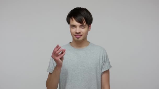 Young enterprising guy with smart gaze showing money gesture and looking cunningly at camera, planning to create passive income, earn more cash for living. studio shot isolated on gray background - Séquence, vidéo
