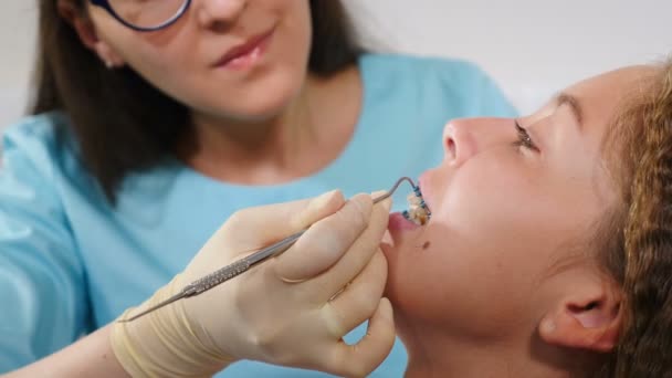Усміхнена жінка-ортодонта вивчає дитину в стоматологічному кабінеті. Крупним планом. Красива дівчина з брекетами на зубах у сучасній стоматологічній клініці. Ортодонтичне лікування. Зуби з зубними дужками. Корекція прикусу
 - Кадри, відео