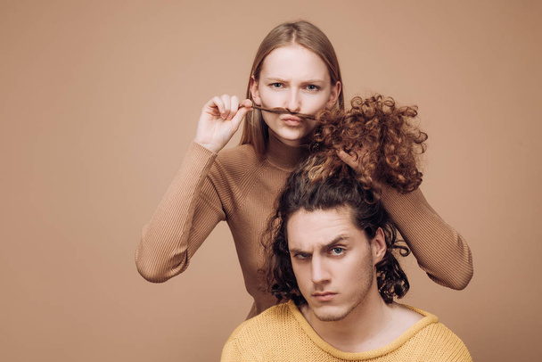Different types of hair concept. Happy couple in love studio photo. Handsome man with long wavy hair and his cute girlfriend. Beautiful girl playing with her boyfriend hair. - Fotó, kép