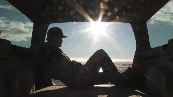 Silhueta do sol, o homem preguiçoso relaxando na parte de trás de seu carro se acalma na praia de areia com sol brilha
. - Filmagem, Vídeo